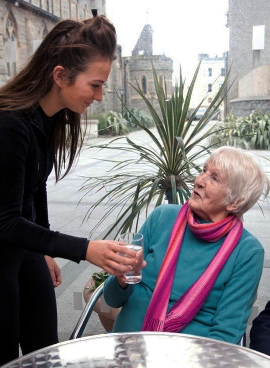 Waitress handing glass of water to elderly customer.